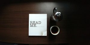 A booklet that says "Read Me" on a table next to a cup of coffee